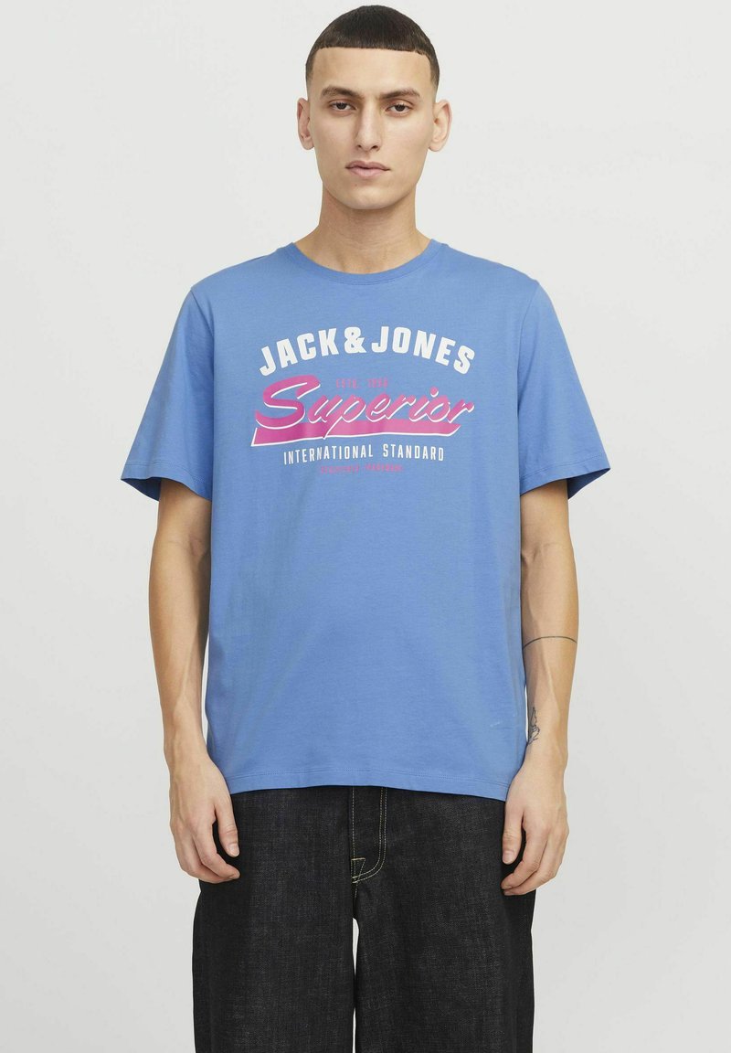 Blå bomulds T-shirt med korte ærmer, der har hvid og lyserød tekst "JACK&JONES Superior" og "INTERNATIONAL STANDARD" på forsiden.