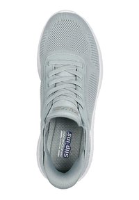 Sneaker atletica grigio chiaro con tomaia in mesh traspirante, lacci piatti, accenti texturizzati e suola in gomma bianca. L'interno presenta un logo stampato.