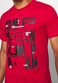 Rood T-shirt van katoen met een ronde hals, voorzien van grote zwarte bedrukte tekst "JUMP" en "MAN" naast een Jumpman-logo.