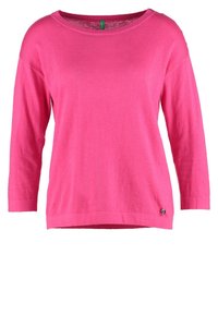 Jasnoróżowy dzianinowy sweter z długim rękawem, okrągłym dekoltem i małym metalowym logo przy krawędzi, prezentowany na białym tle.