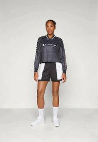 Fekete, cropped hosszú ujjú póló "Champion" logóval, hálós textúrával és grafikai részletekkel az ujjakon; fekete-fehér sportnadrággal párosítva.