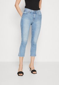 Pantalones vaqueros cortos de color azul claro con un diseño ajustado, que presentan una cinturilla de altura media y un ligero deshilachado en el dobladillo. Llevados con sandalias de tacón negras.
