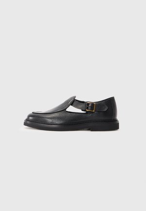 Black leather T-bar shoe with a textured finish, featuring a buckle strap and a rounded toe. Low, sturdy black sole.