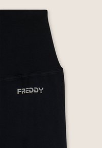 Sezione di indumento nero a vita alta con texture a righe orizzontali e logo "FREDDY" in lettering bianco.