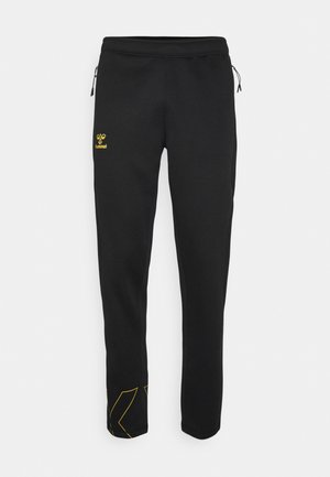 Pantaloni della tuta neri realizzati in materiale morbido. Presentano un logo giallo e dettagli a contrasto alla caviglia. Inclusi di cordoncino regolabile in vita.
