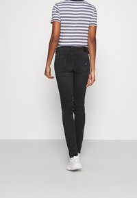 Jeans negros ajustados con una cintura de altura media, combinados con una camiseta a rayas gris y blanca. El conjunto presenta un diseño minimalista.