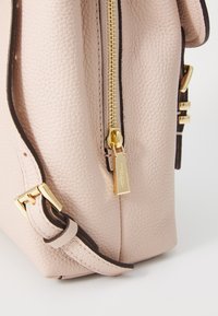 Roze leren handtas met een gepebbelde structuur, een gouden rits, donkerbruine accenten, een verstelbare schouderband en een metalen logo-detail nabij de rits.