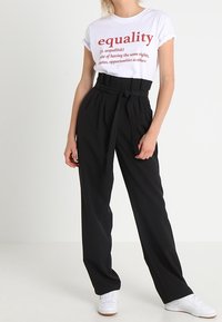 T-shirt blanc avec du texte rouge indiquant "égalité", associé à un pantalon noir ample taille haute et des baskets blanches.