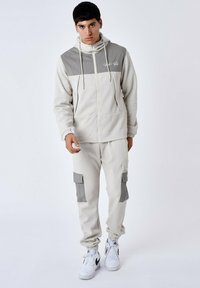 Lichtgrijze zip-up hoodie met een textuurpaneel in grijs en koordjes, gecombineerd met bijpassende cargobroek met grijze accenten en zakken.