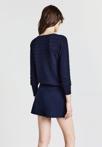 Pull-over en maille bleu marine avec un motif géométrique, manches trois quarts, associé à un short bleu marine. Les deux pièces ont une finition lisse.