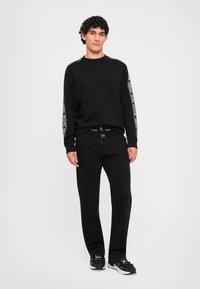 Melna sporta krekls ar baltām sānu svītrām, melnas bikses un melnas apavus. Apģērbs izceļas ar brīvu piegriezumu un kontrastējošiem šuvju detalizējumiem.