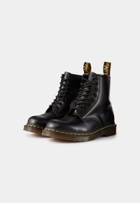 Bottines en cuir noir avec des coutures jaunes et deux languettes de tirage. Présente un bout arrondi et un design à lacets. Semelle en caoutchouc texturée.