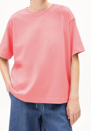 T-shirt en coton rose avec un col rond, des épaules tombantes et une coupe décontractée. Associée à un short en denim ample, doté de détails de couture visibles.