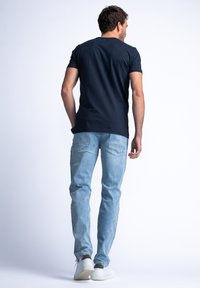 Marineblauwe t-shirt met korte mouwen, gecombineerd met lichte spijkerbroek en witte sneakers. Zachte stof, ontspannen pasvorm en recht model.