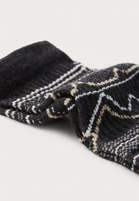 Calcetín negro de punto con una textura suave, que presenta patrones geométricos en blanco y beige y un puño acanalado para mayor sujeción.