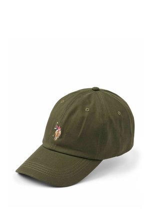 Smilende kvinde med langt blondt hår, iført en olivengrøn kasket med en polo-spillerlogo og en lysegrå skjorte.