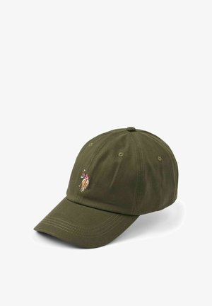 Lächelnde Frau mit langen blonden Haaren, die eine olivgrüne Kappe mit einem Polospieler-Logo und ein hellgraues Hemd trägt.