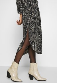 Abito nero con motivo floreale bianco, spacchi laterali, abbinato a stivaletti alla caviglia in finta pelle beige con finitura texture e tacco squadrato.