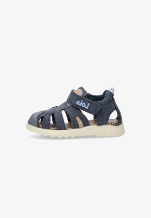 Sandalía azul oscuro con los laterales abiertos, correas texturizadas, cierre de Velcro ajustable, suela beige y plantilla suave con un patrón colorido.