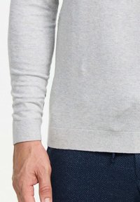 Helles grauer Langarmpullover mit gerippten B�ündchen und Saum, aus weichem Stoff, kombiniert mit dunkel strukturierten Hosen.