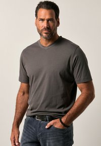Camiseta gris de cuello en V en tejido suave, con mangas cortas y un branding sutil. Combinada con unos vaqueros azul oscuro y un cinturón negro con un acento trenzado.