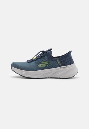 Zapato deportivo azul marino con parte superior de punto, media suela blanca y detalle texturizado en el talón. Cordones elásticos con cierre ajustable de pestillo.