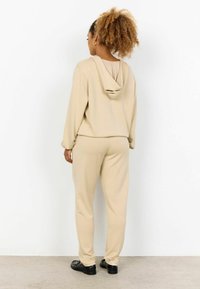 Felpa beige con cappuccio e pantaloni coordinati, realizzati in tessuto morbido. Presenta un cappuccio, polsini a coste sulle maniche e sui polsini delle caviglie, con una vestibilità rilassata.