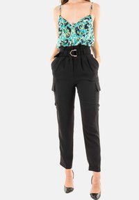 Pantalones cargo negros de cintura alta con bolsillos frontales, combinados con un top de tirantes delgados de color azul y verde con un patrón y accesorios decorativos.