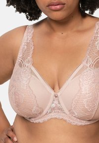 Różowy koronkowy biustonosz z kwiatowymi wzorami, siateczkowymi panelami i ozdobną kokardką na środku. Szerokie ramiączka i misterna koronka podkreślają szczegóły.