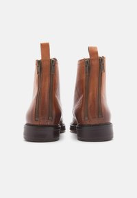 Botas de cuero marrón hasta el tobillo con dos cremalleras laterales, una tira en la parte trasera y una suela oscura contrastante. Textura suave con un diseño minimalista.