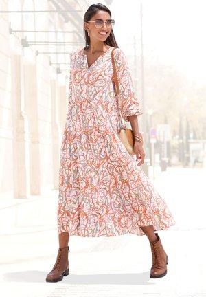 Maxikleid mit einem floralem Muster in Pink, Orange und Grün, mit langen Ärmeln, einem V-Ausschnitt und einem gestuften Design. Braune Schnürstiefel.