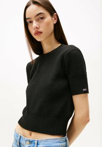 Maglione corto nero a coste con maniche corte e finitura texturizzata. Presenta un piccolo logo sulla manica sinistra.