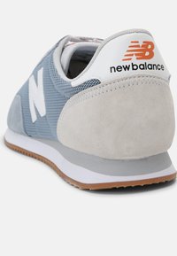 Vista posteriore di una sneaker New Balance blu chiaro e grigia con suola bianca e logo arancione sul tab del tallone.