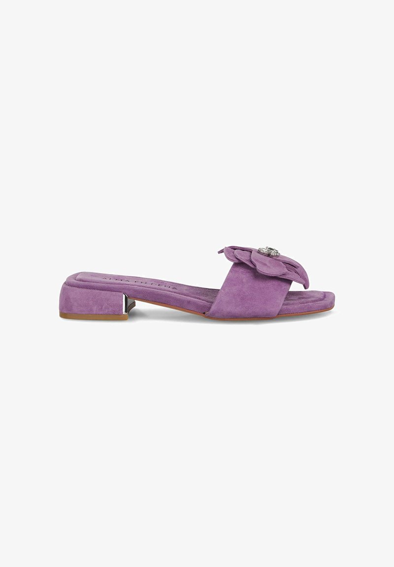 Sandal de ante morado con un bajo tacón cuadrado y un gran adorno de flor de tela decorado con un strass. Suela plana, diseño de punta abierta.