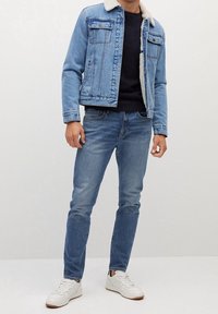 Chaqueta de denim con forro de sherpa, color azul claro, dos bolsillos en el pecho, combinada con jeans azul claro y zapatillas blancas. Diseño simple, corte casual.