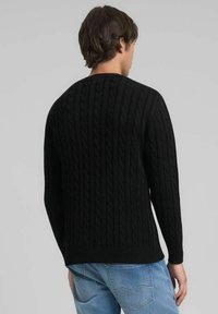 Pull noir en maille avec un motif torsadé, poignets et ourlet côtelés, doté d'un col rond classique. Porté avec un denim bleu clair.