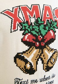 Gebreide trui met een crèmekleurige achtergrond met de tekst "XMAS", rode accenten, groene hulstbladeren en bruine bellen met witte highlights eronder.