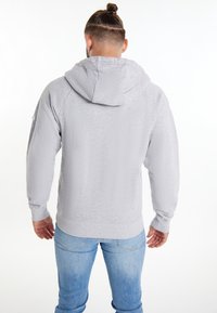 Sweat à capuche gris clair avec une finition texturée, manches longues et ourlet côtelé, associé à un jean en denim bleu.