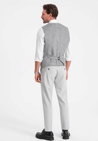 Chaleco a cuadros gris con espalda ajustable, usado sobre una camisa blanca. Combinado con pantalones gris claro y zapatos negros de cordones.