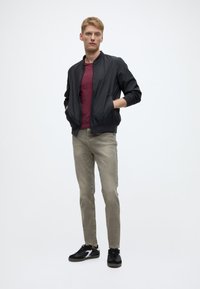 Juoda bombonešio striukė, bordo spalvos marškinėliai, šviesiai pilki džinsai ir juodi sportbačiai. Bombonešio striukė pasižymi lygiu audiniu ir elastingomis rankogalių apvadėlėmis su kišenėmis.