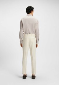 Vaaleanbeige paita, jossa on hillitty geometrinen kuvio, yhdistettynä kermanvärisiin housuihin, joissa on molemmissa räätälöity istuvuus ja sileä kangas.