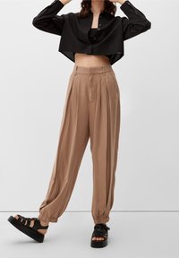 Zwarte gecropte blouse met knopen gecombineerd met brede, geplooide beige broeken en zwarte plateau sandalen, wat een ontspannen pasvorm en zachte stof benadrukt.