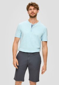 Chemise henley à manches courtes bleu clair avec un col rond et une patte de boutonnage à trois boutons, assortie à un short gris foncé avec des poches latérales.
