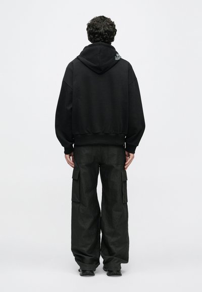 Hanorac negru supradimensionat cu un buzunar frontal și șnururi, asortat cu pantaloni cargo negri, largi, cu buzunare laterale.