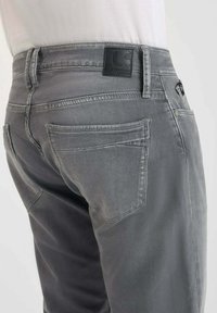 Pantalones de mezclilla gris con una textura suave, diseño de cinco bolsillos y un parche de cuero negro de la marca en la cinturilla.