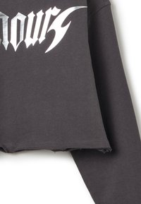 Donkergrijze cropped sweatshirt met lange mouwen, voorzien van een metallic zilveren grafisch ontwerp. De zoom heeft een verouderde rand voor een ruwe uitstraling.