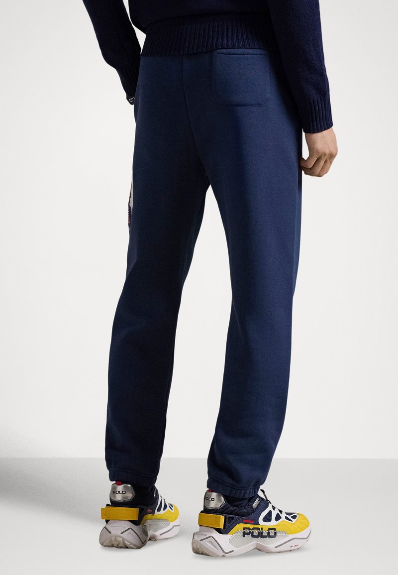 Pantalon de survêtement bleu marine à coupe fuselée, avec une taille texturée et une poche arrière. Associé à des baskets multicolores avec des accents de marque.