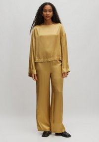 Goldsatin-Loungewear-Set mit einem kurzärmeligen Top und weiten, lockeren Hosen. Glatte Textur mit sanftem Schimmer, minimalen Nähten und ohne sichtbare Muster.