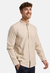 Camisa de botones en algodón de color beige claro. Presenta un collar, botones frontales y mangas largas con puños abotonados. Detalle de costura simple.