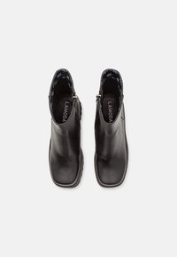 Paire de bottines en cuir noir avec bouts carrés et fermetures éclair latérales, vues de dessus sur fond blanc.